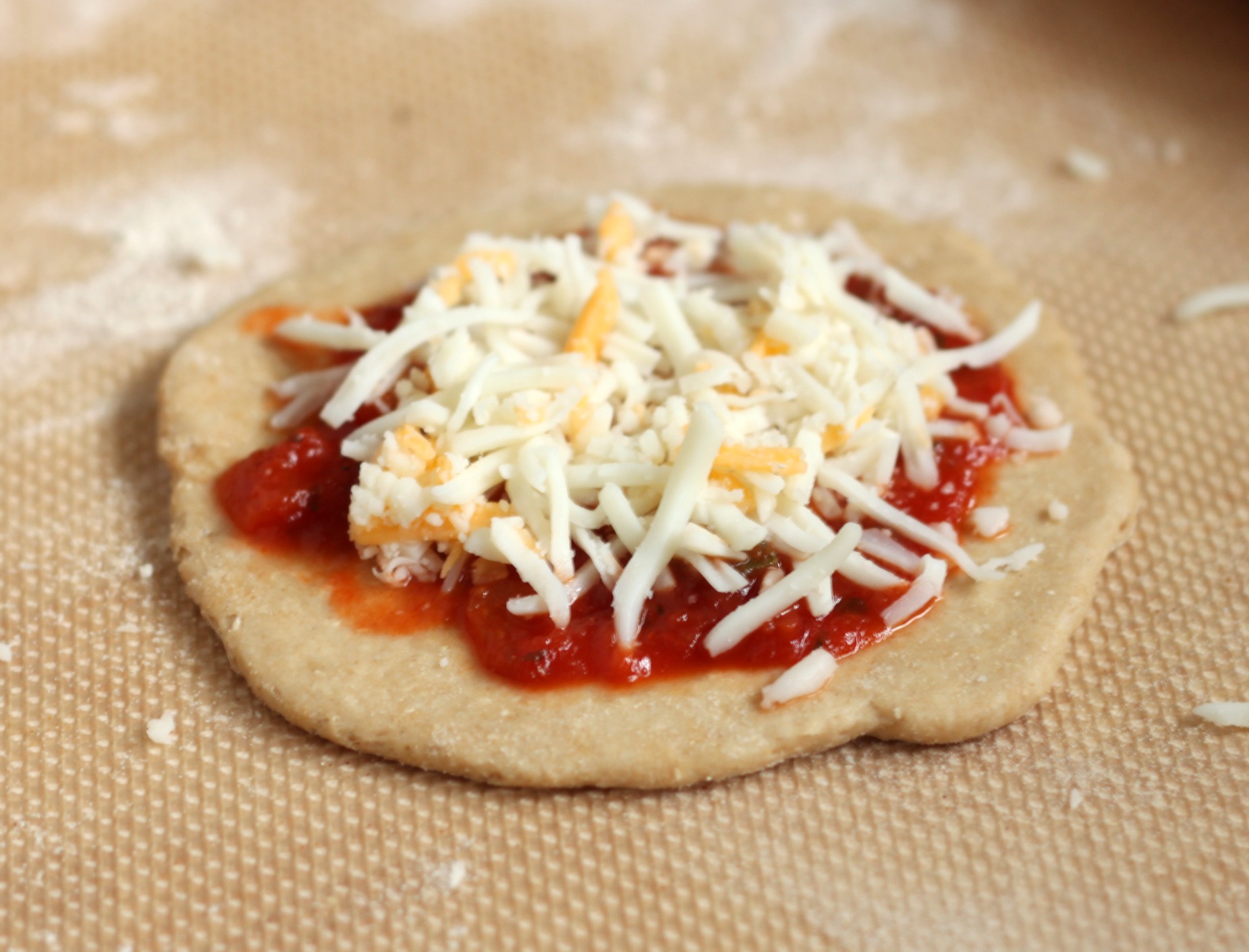 Add sauce and cheese to pizza dough cropped